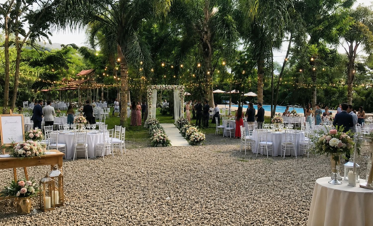 Boda al aire libre con mesas blancas y luces colgantes entre las palmeras